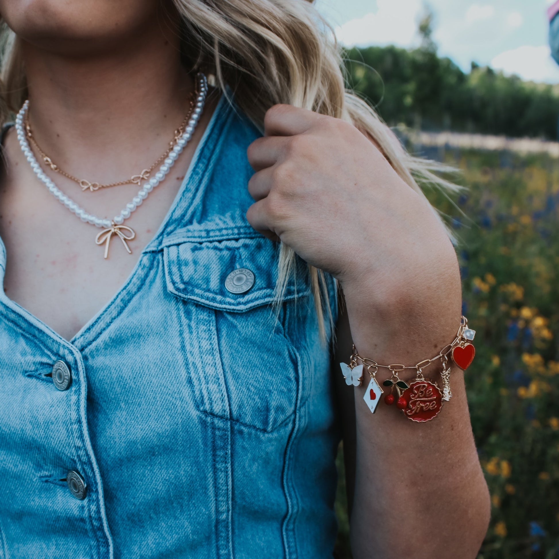 Person wearing a denim vest with jewelry in a natural setting charm bracelet red cherry