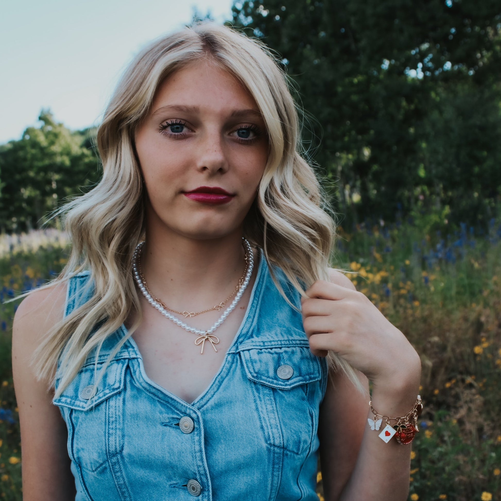 Woman in a denim vest standing in a field with wildflowers and trees in the background