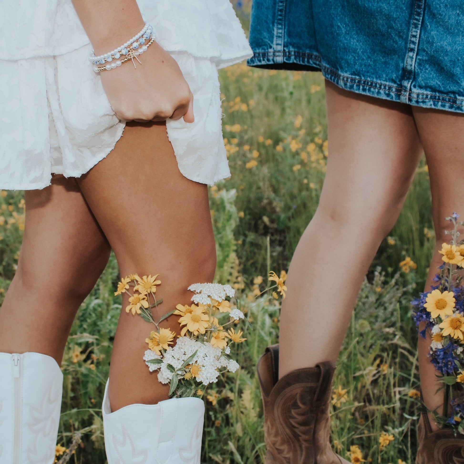 Two people standing in a field of flowers, wearing white boots and denim shorts. Charm bracelets porcelain bracelets pearls gold