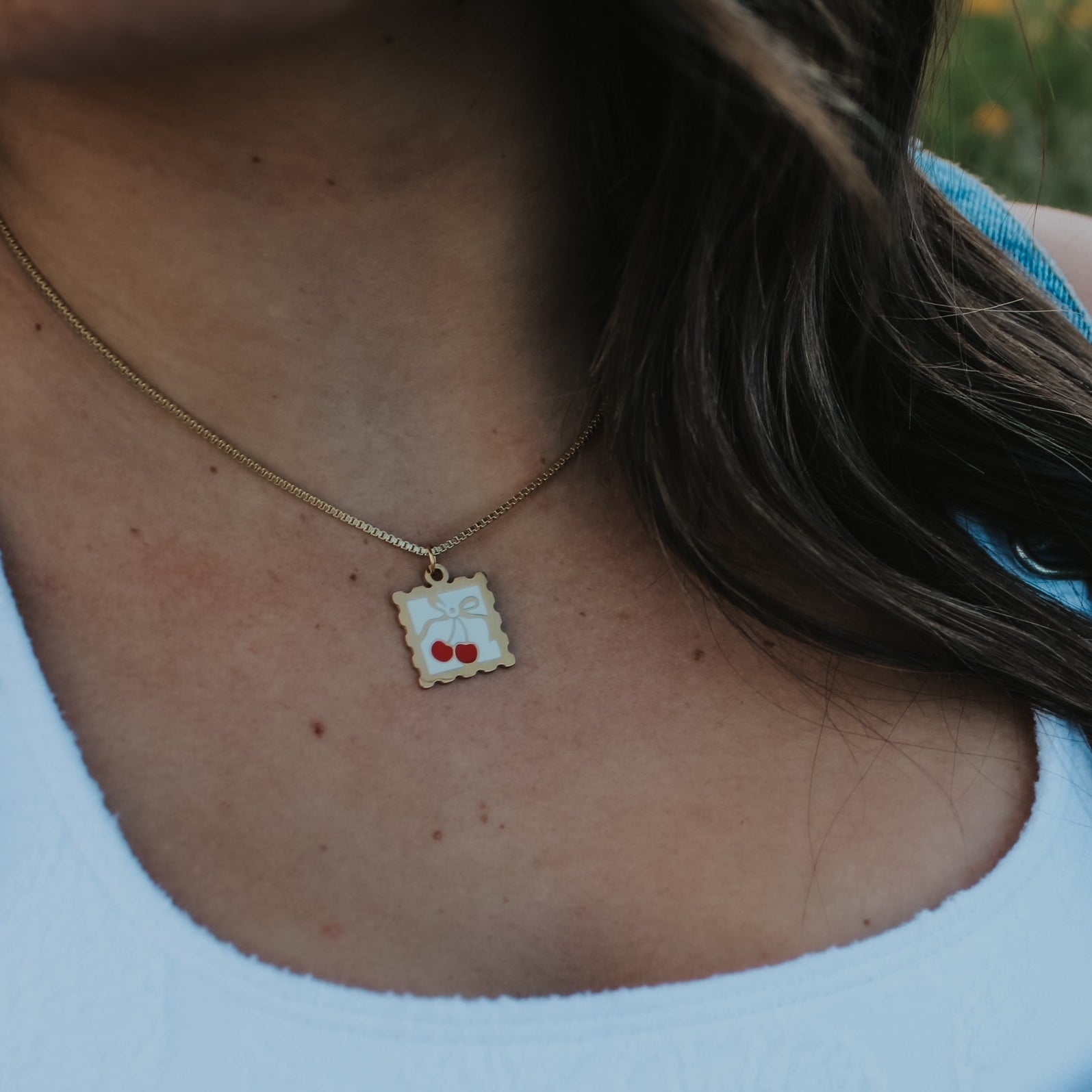 Person wearing a necklace with a small pendant, standing outdoors with blurred background
